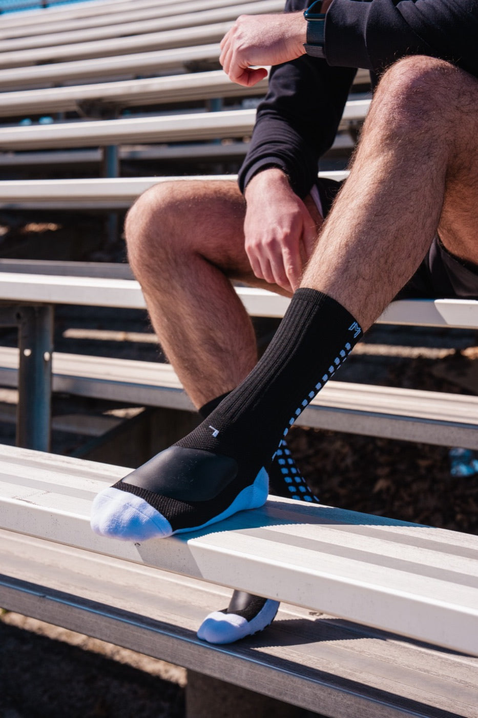Black MediCaptain padded grip sock on a bleacher bench, ShockPad visible over the top of the foot