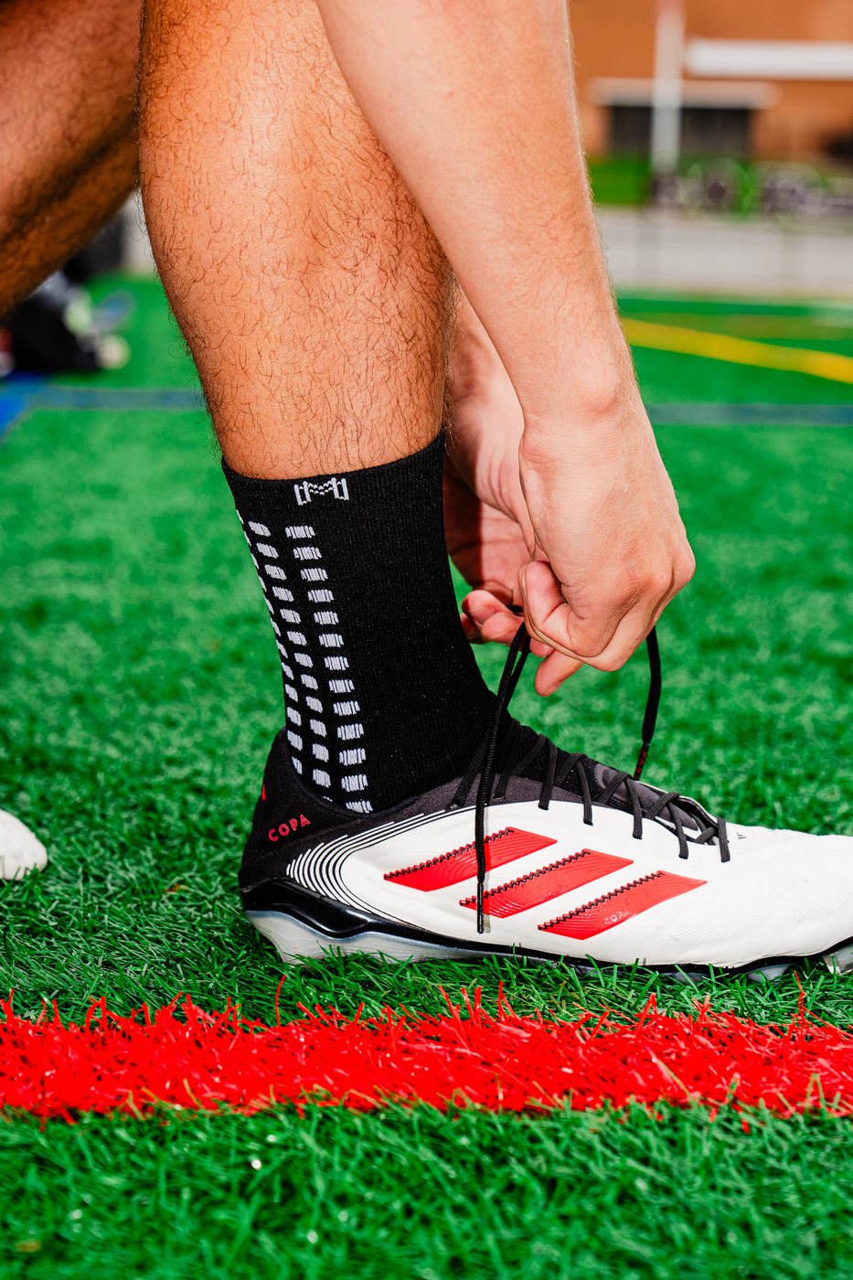 Close-up of a player lacing a cleat wearing black MediCaptain grip socks, grip pattern visible